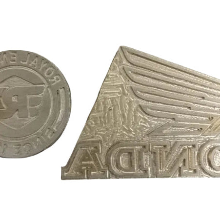 Two metallic emblems with intricate designs on a dark surface